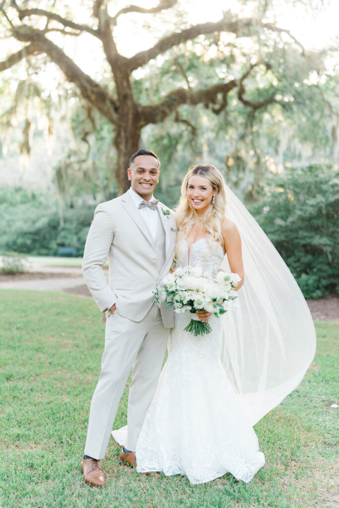 Wedding day portrait of bride and groom with veil blowing in the wind. Groom in tan 3 piece suit and patterned bow tie. Intimate weddings in Charleston, SC.