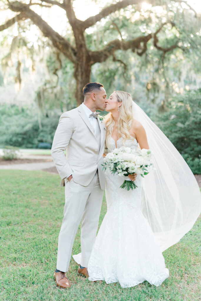 Bride and groom kissing white sunshine and spanish moss in background. Wedding photographers in Charleston. 