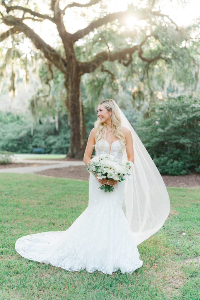 Wedding day Charleston bridal portraits. Bride standing and looking off to the side. Long blonde hair. Live oak tree and spanish moss in background. 