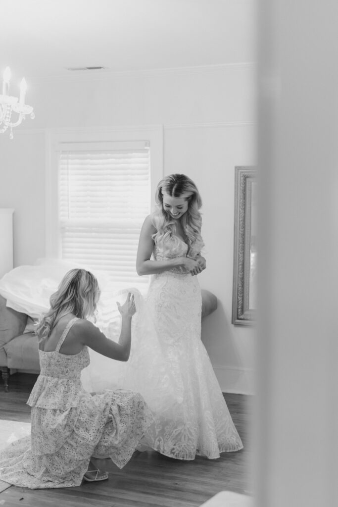 Black and white photo of bride getting ready with help from her sister. 