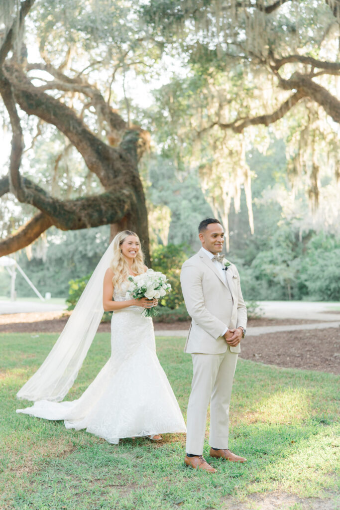 Groom in tan suit. First look with bride. Bride walks up to tap groom on the shoulder. Old live oak trees and sun-kissed spanish moss. intimate charleston elopement.