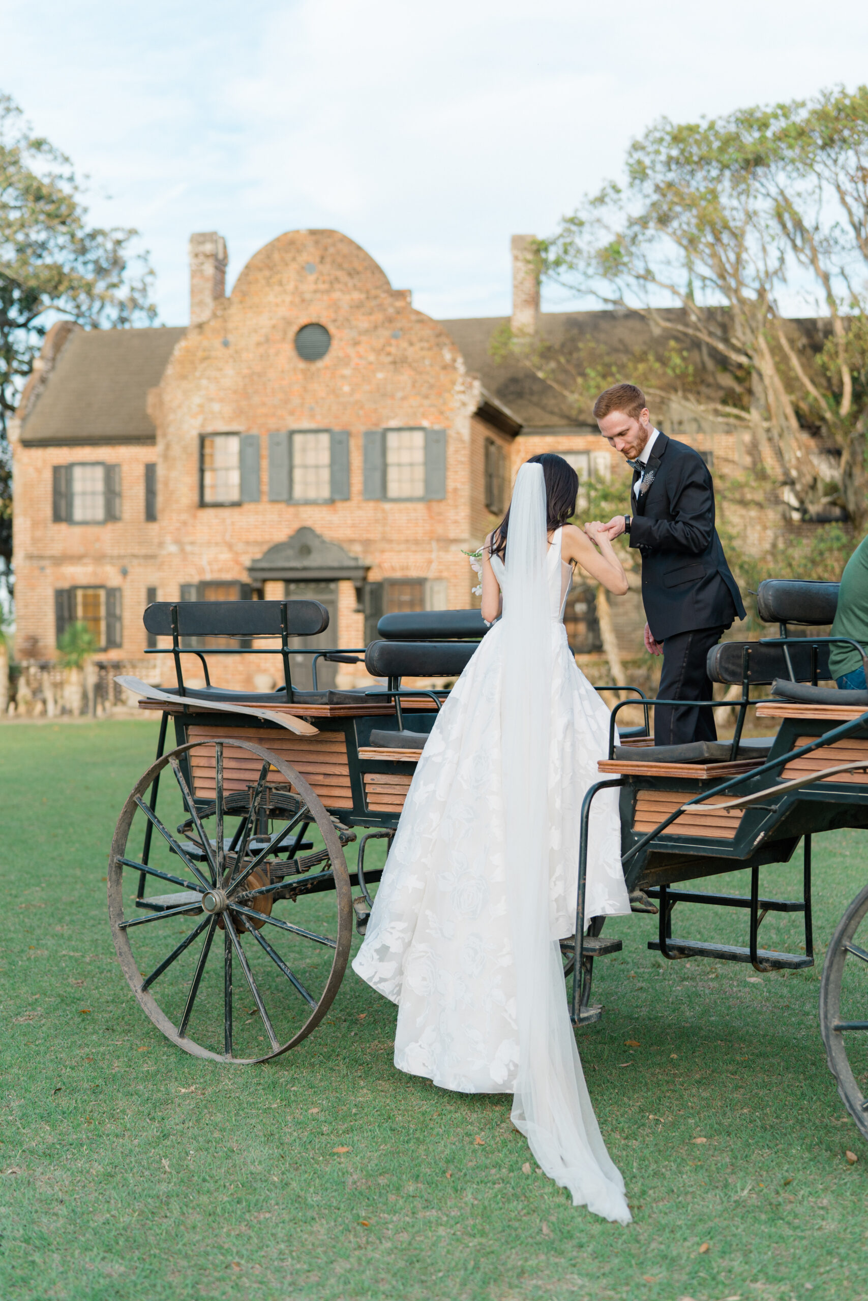 Groom helps bride get on carriage. Horse and carriage ride after wedding ceremony at Charleston wedding.