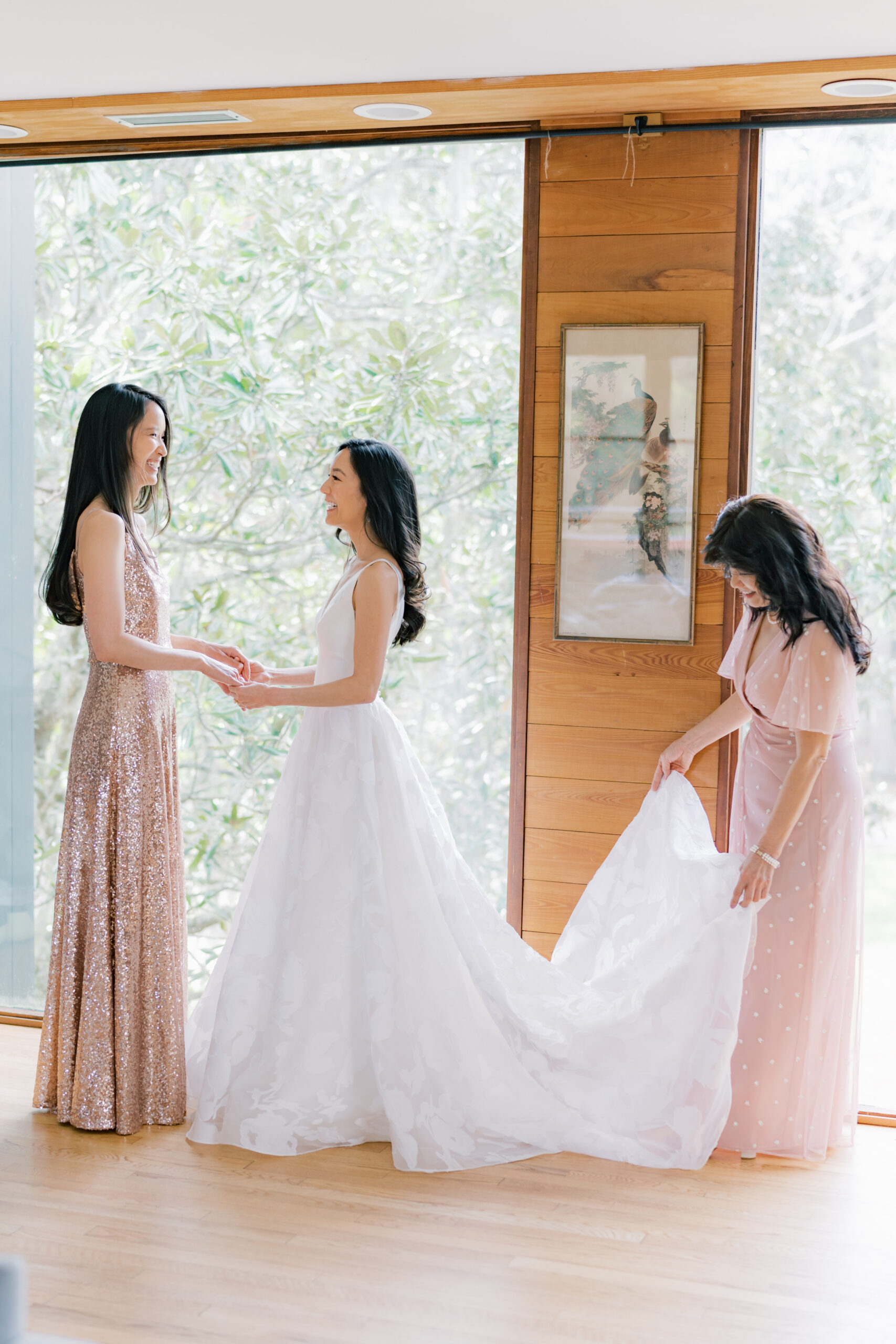 Bride holding hands with her sister while her mom spread out her wedding dress. 