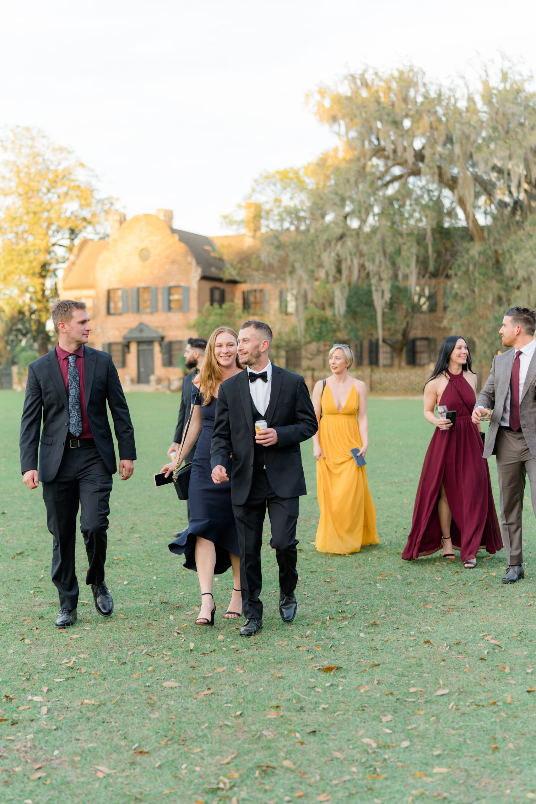 Wedding guests walk on the lawn at Middleton Place. Matching tones wedding guest outfits. 