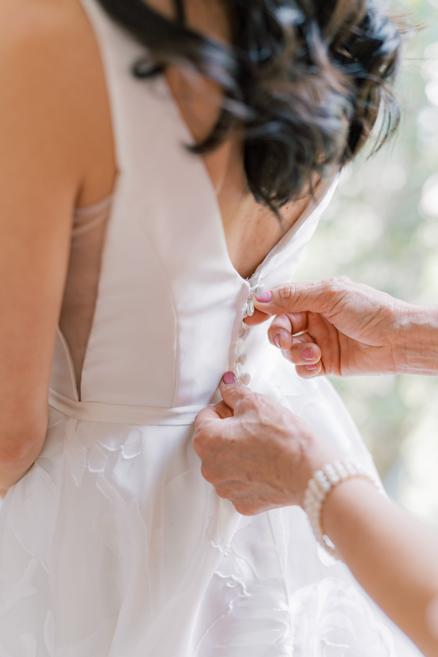 Mother of the bride buttons up her daughters wedding dress. 