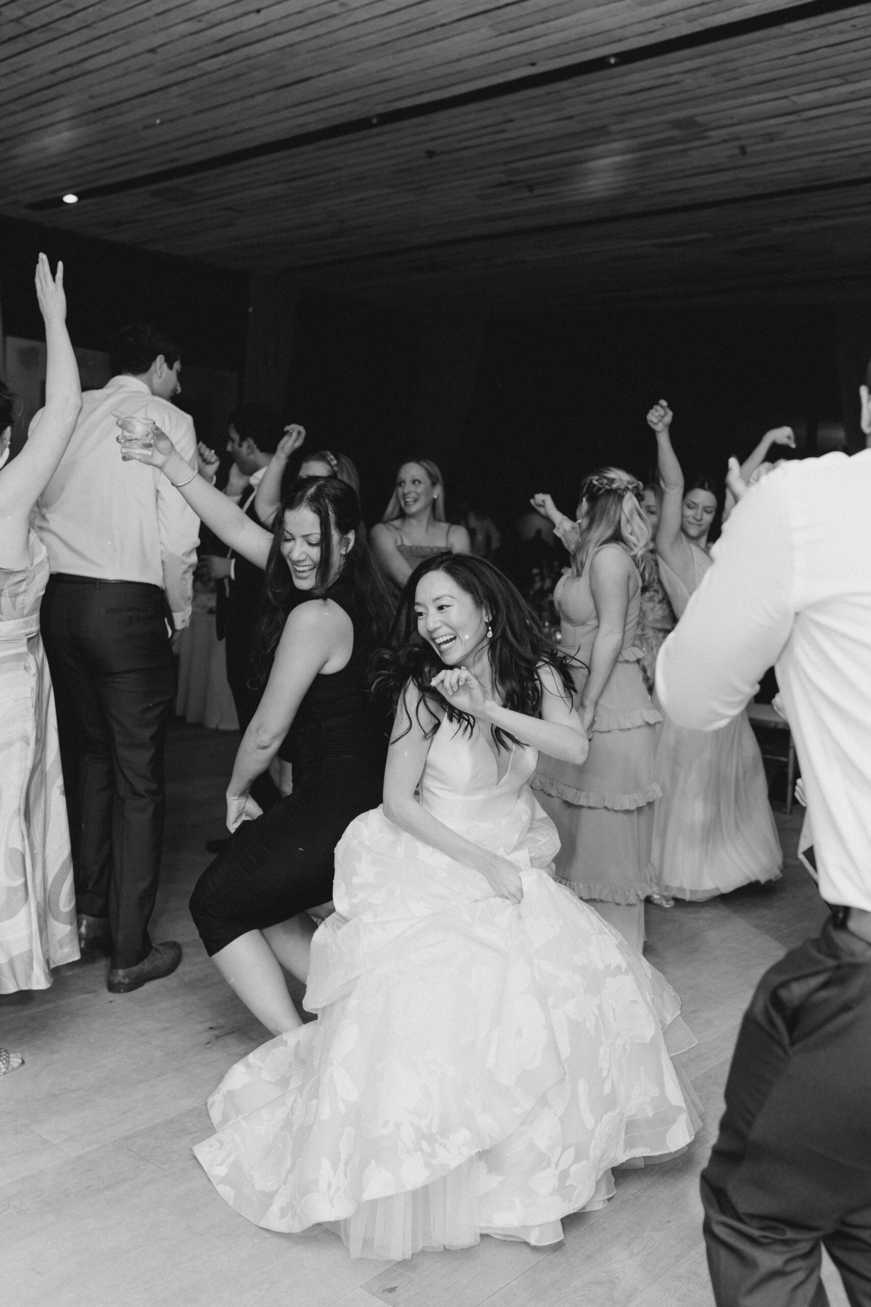 Black and white wedding photo of bride dancing back to back with her friend on the dance floor. 