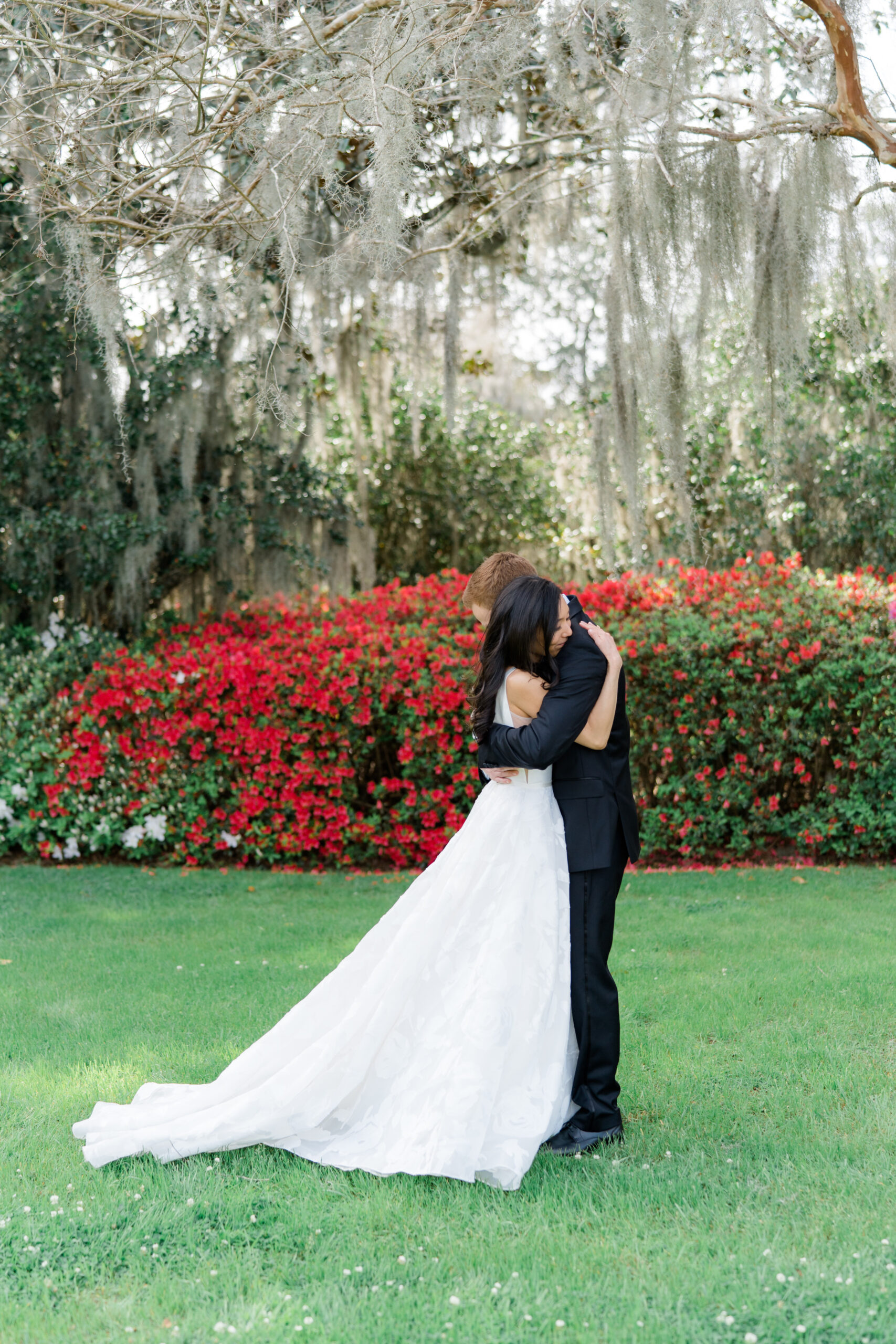 Bride and groom hug during first look.   Spanish moss and red azalea blooms. 