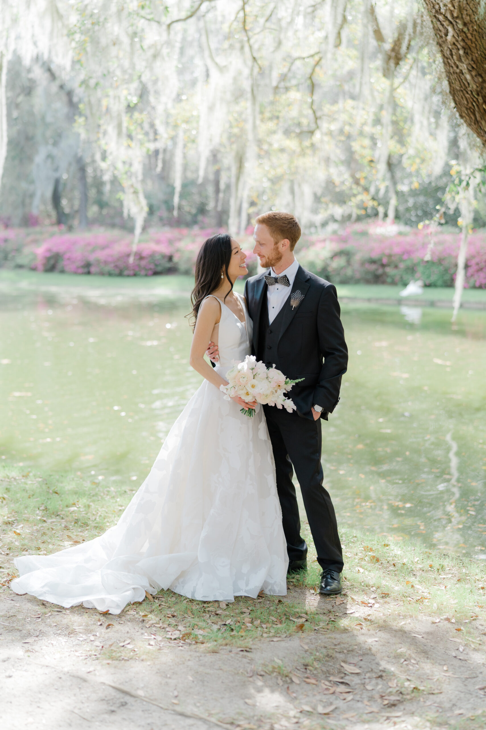Bride and groom portraits by the pond at Middleton Place with pink azalea blooms in the background.