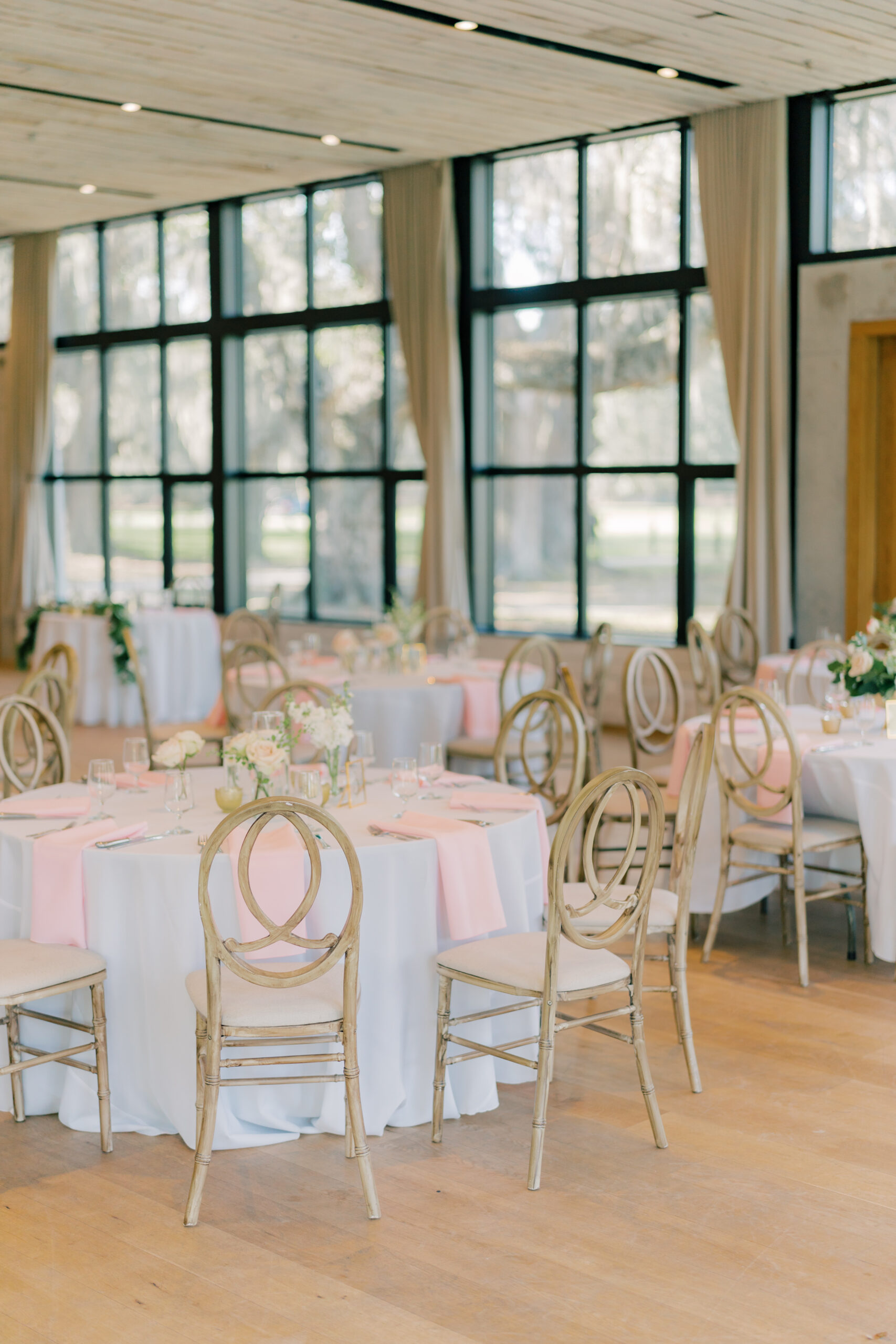 Simple wedding reception set up. White table linens with pink napkins, and small centerpieces.