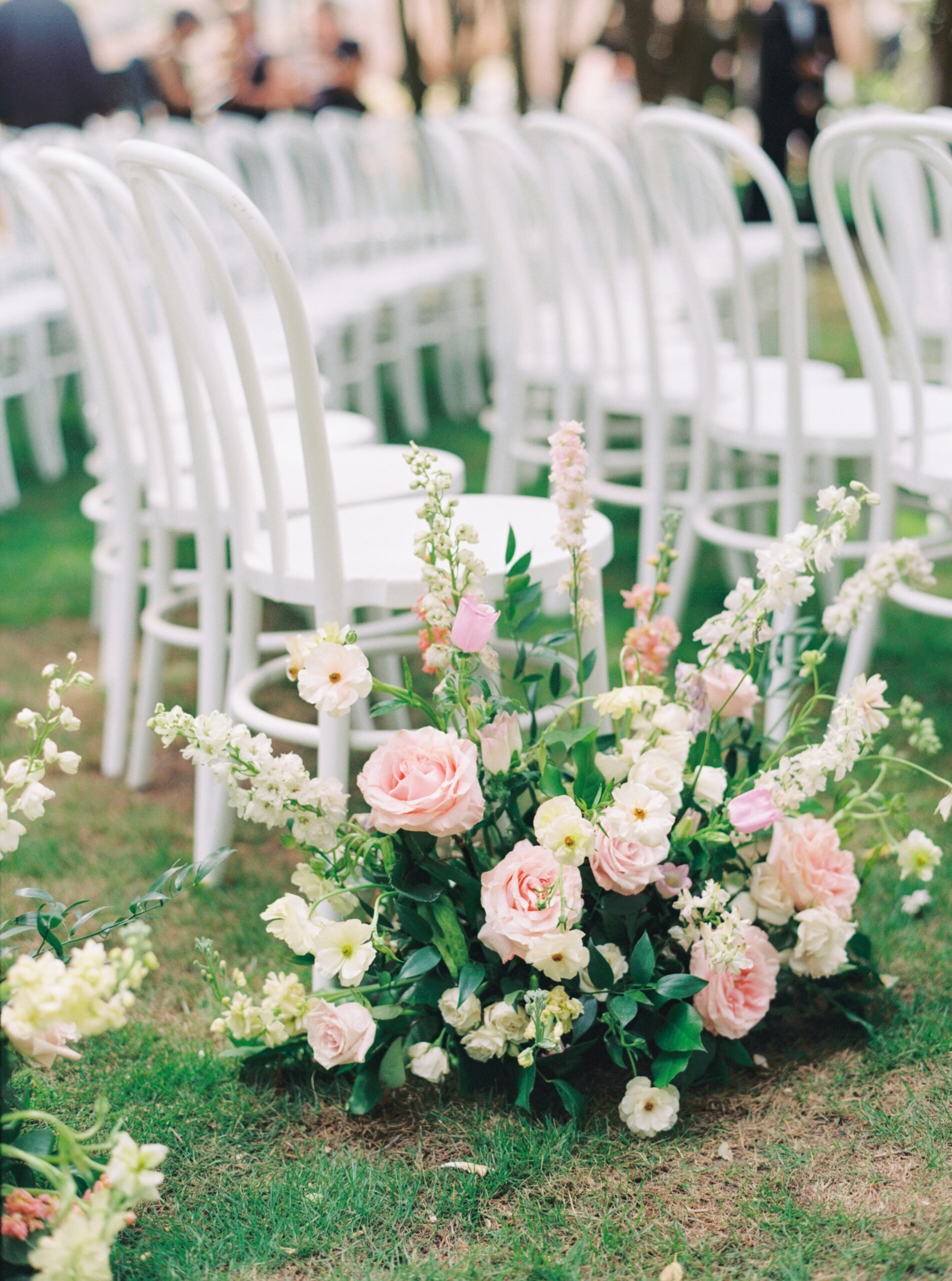 White and pink wedding ceremony aisle flowers with white chairs.