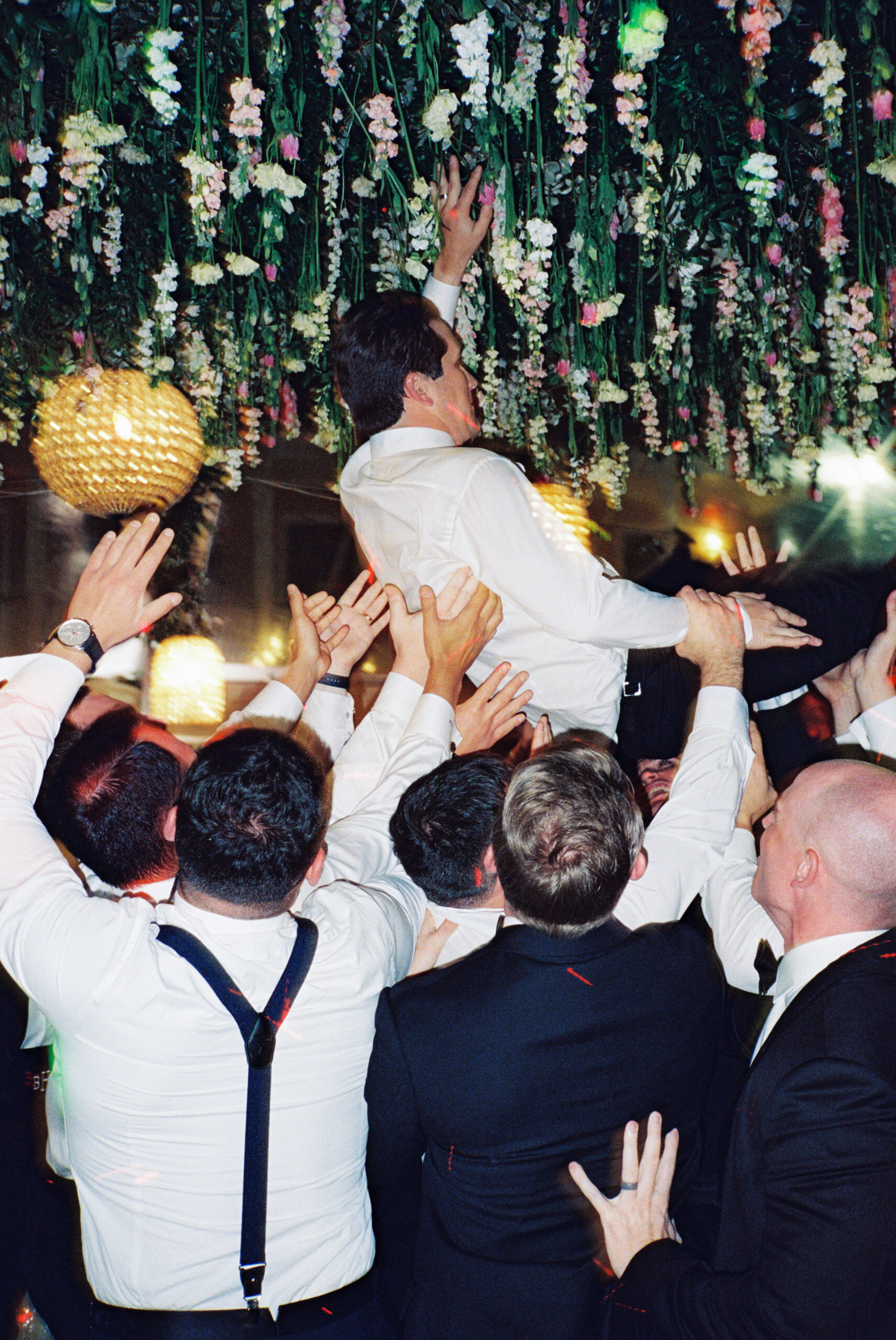 Flash film photo of groom getting carried by wedding guests.