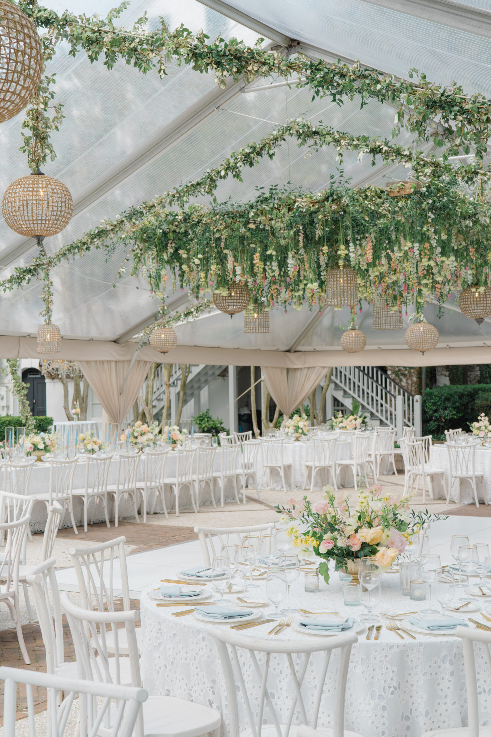 White eye-hole table cloth and white chairs with soft pastel flowers. Birdcage lighting on hanging floral installation. 