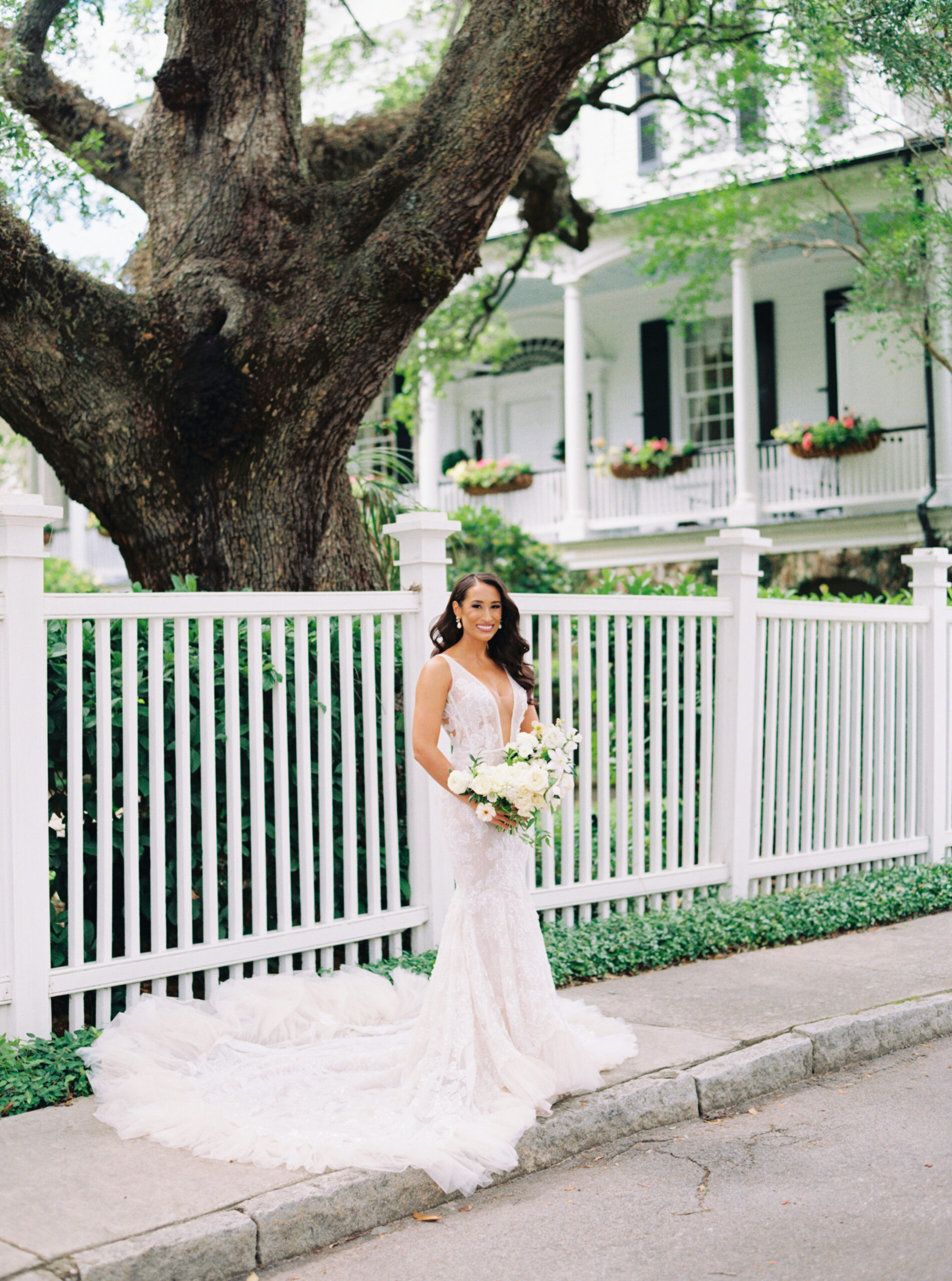 Film photo wedding photographer. Bride standing on the sidewalk in front of white fence.