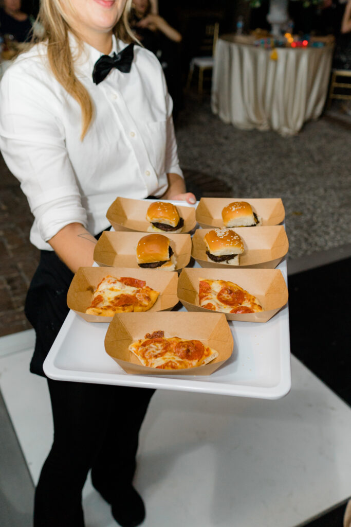 Late night burgers and pizza held on a tray by servers. 