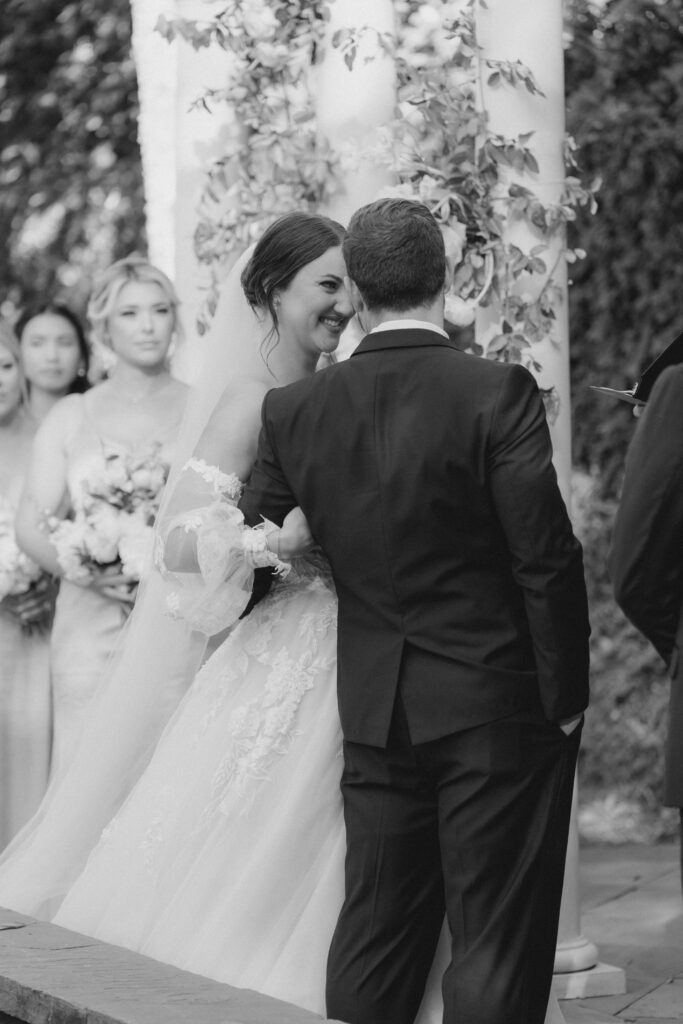 Bride smiles at groom during wedding ceremony. Black and white wedding photo.