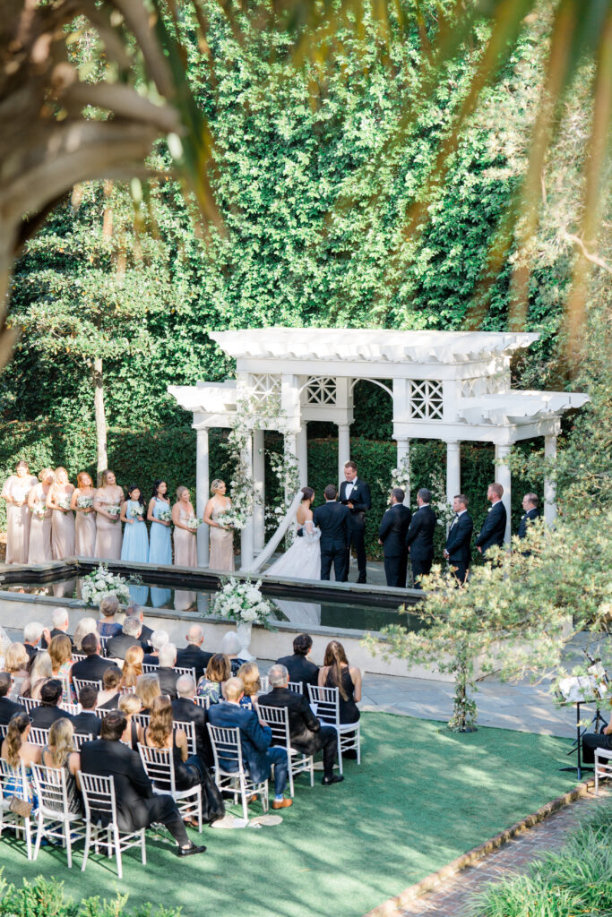 Overall photo of garden wedding ceremony in Charleston SC. White arbor and greenery.