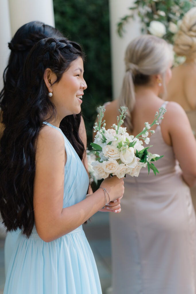Junior bridesmaid in light blue dress smiles during wedding ceremony. 