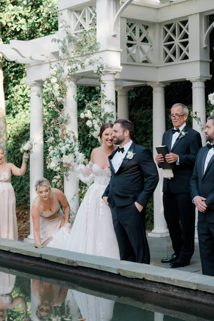 Just married. Bride smiles at groom after turning around. Maid of Honor helps with dress. Cute moments captured at wedding ceremony. 