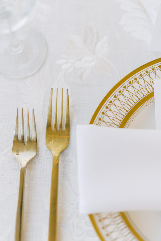 Close up of white and gold place setting at spring wedding.