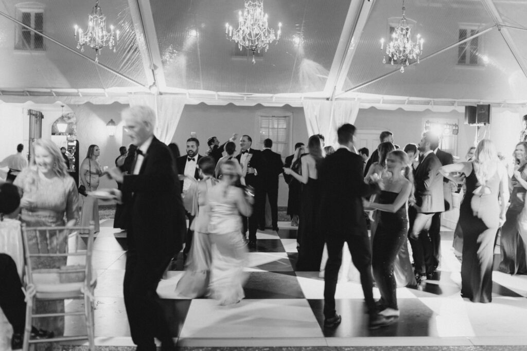 Black and white motion blur of dance floor at Charleston outdoor tented wedding reception with chandeliers. 