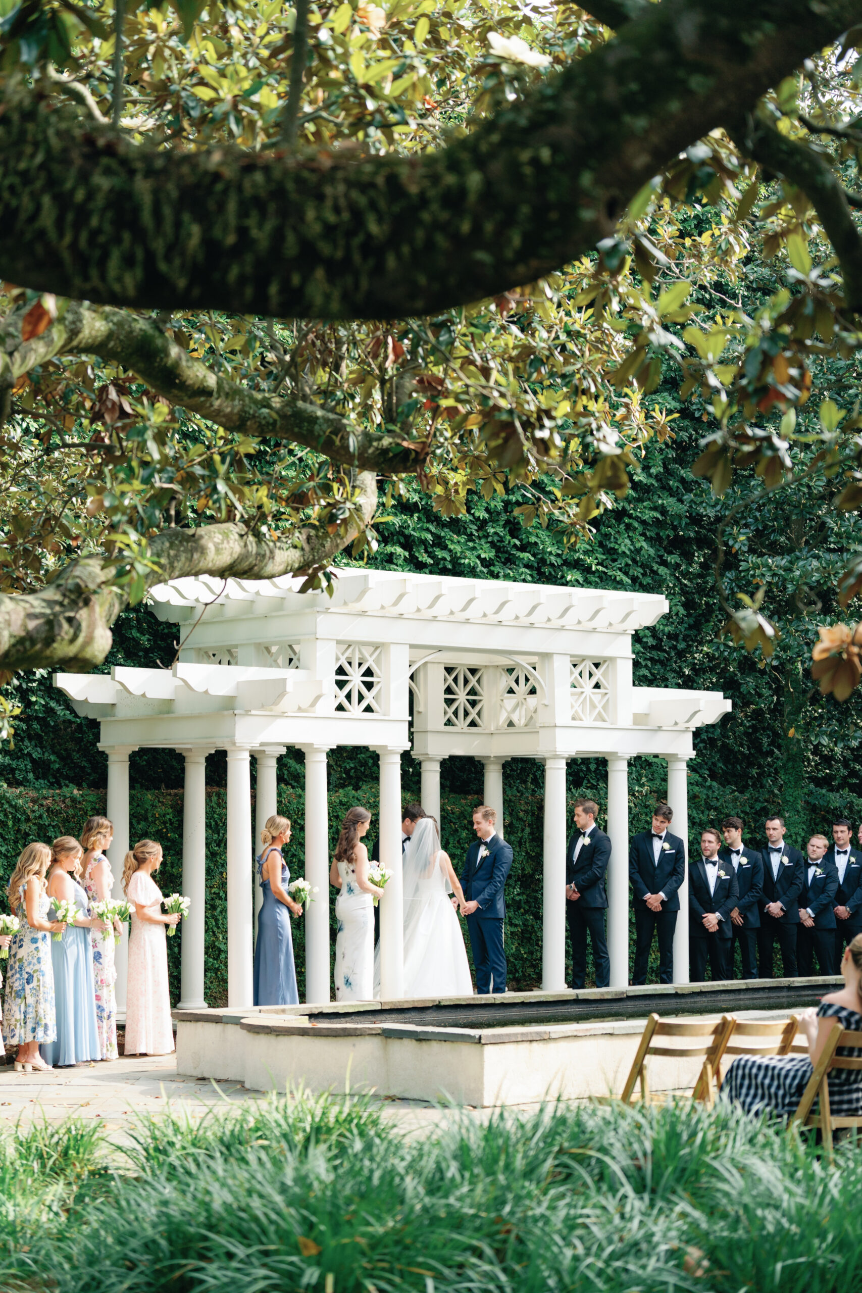Wedding ceremony under the white arbor in the garden at William Aiken House. 