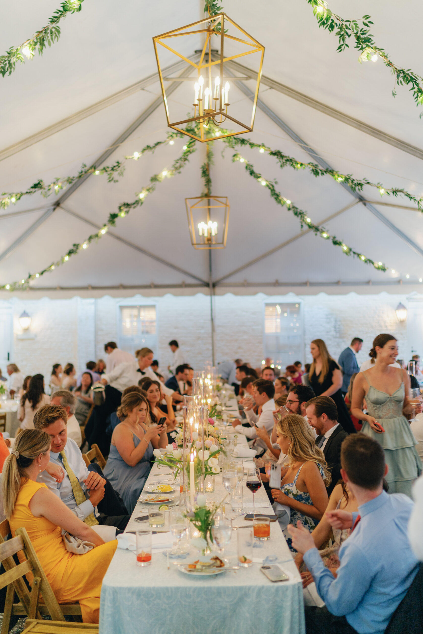 Dinner time at Charleston spring wedding reception. Hanging greenery and string lights with gold box modern chandeliers. 