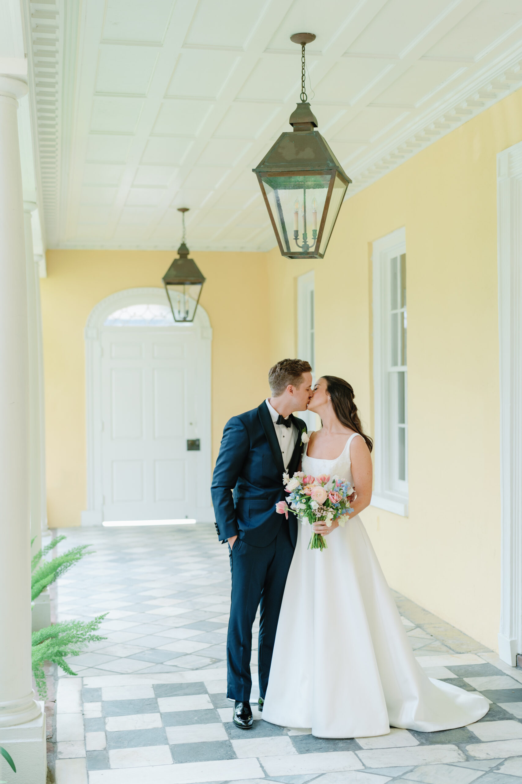 Bride and groom kiss under gas lanterns on checkerboard floor. Charleston destination wedding.
