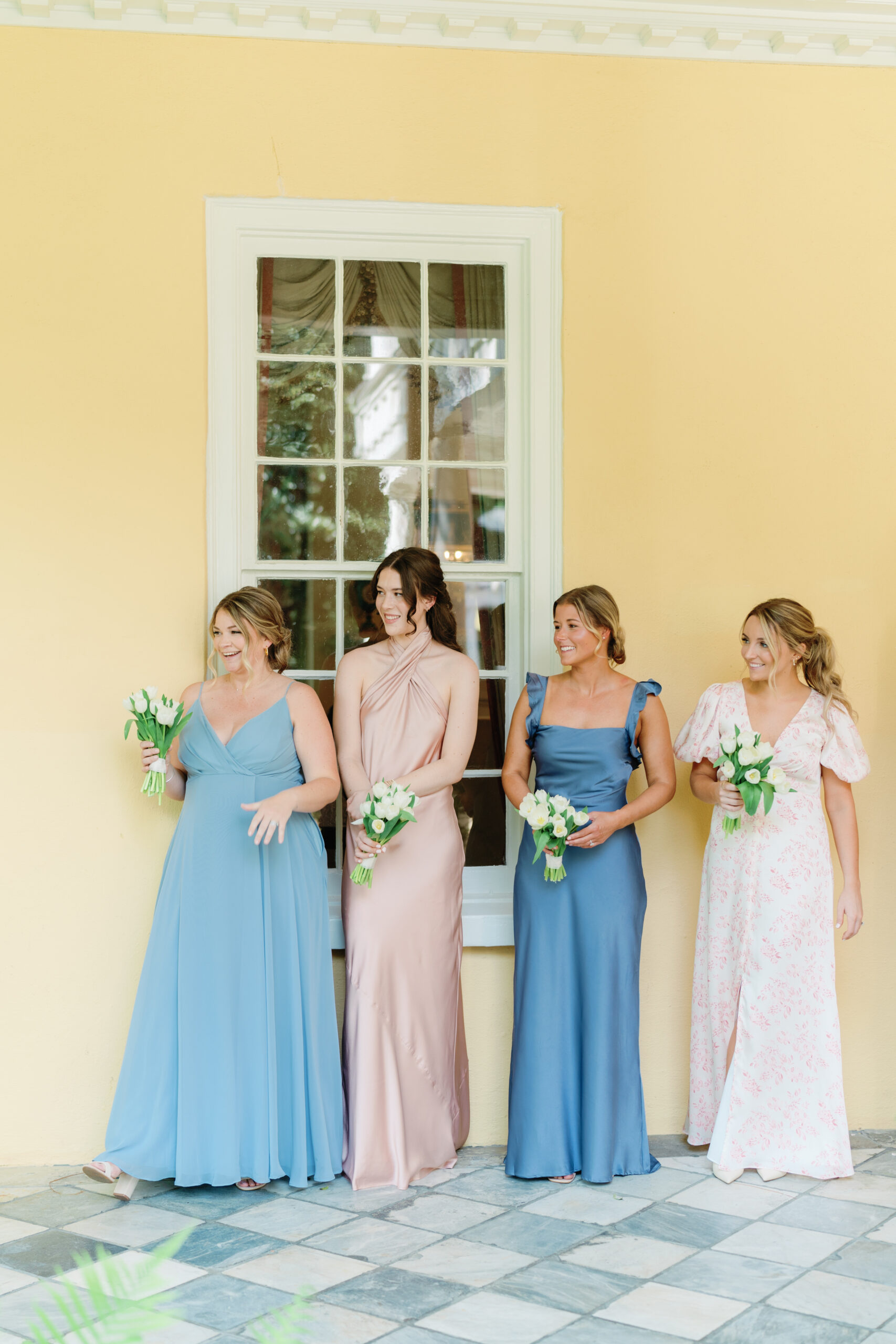 Bridesmaids in mix-matched dresses watching the bride get portraits taken. Charleston wedding photographer. 