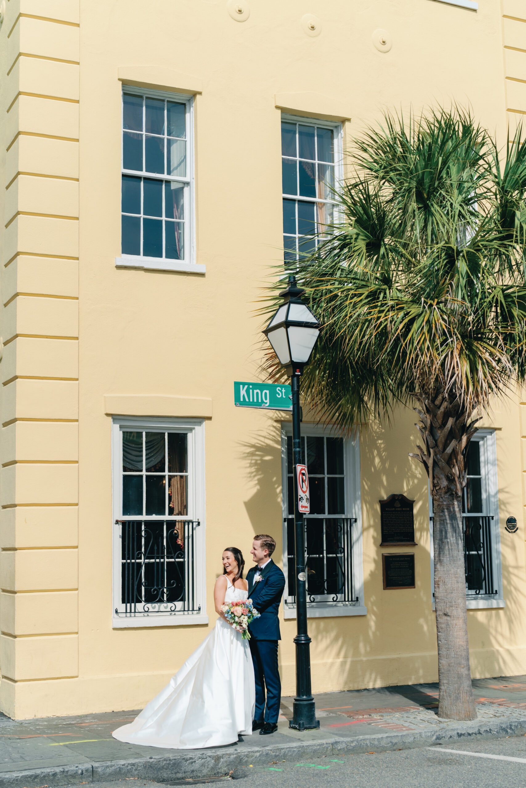 Bride and groom laugh with people walking by on King Street in downtown Charleston. 