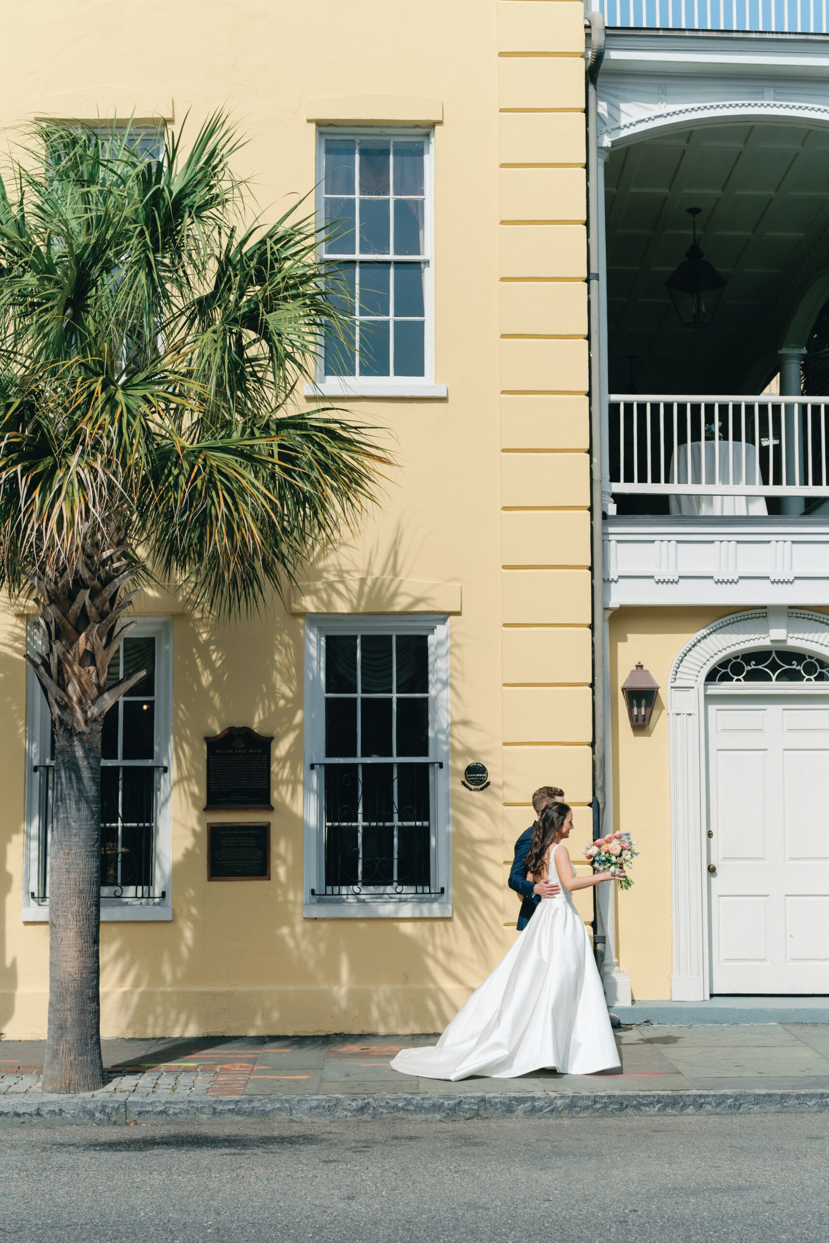 Groom puts his arm around bride while walking down the street in downtown Charleston. Palm tree.