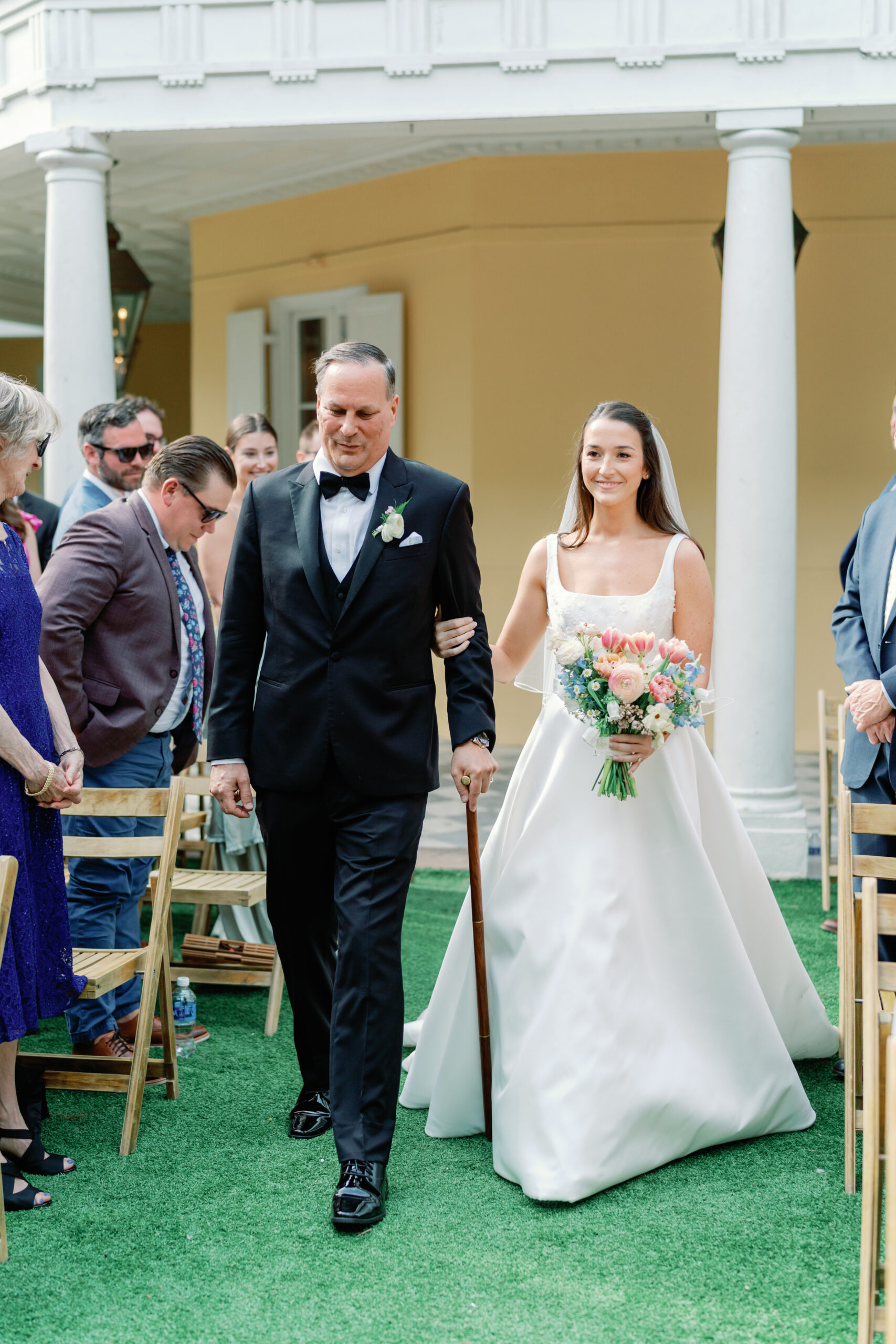 Bride walking up the aisle escorted by her dad with a cane. 