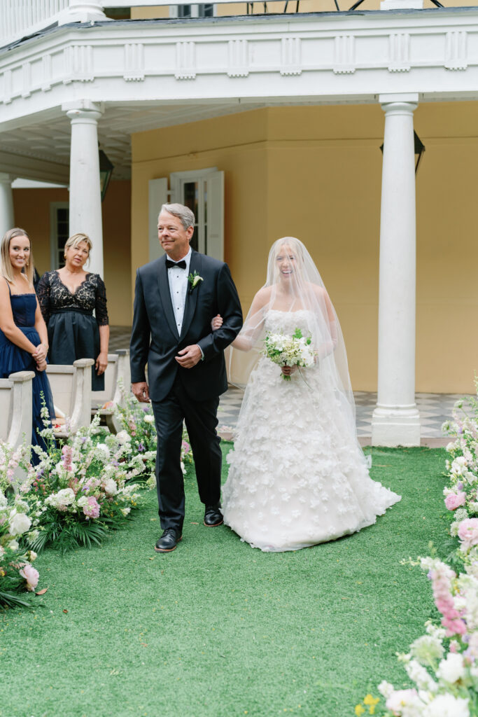 Covered in a veil, bride smiles at groom walking up the aisle at spring wedding ceremony in charleston. charleston photographer wedding.
