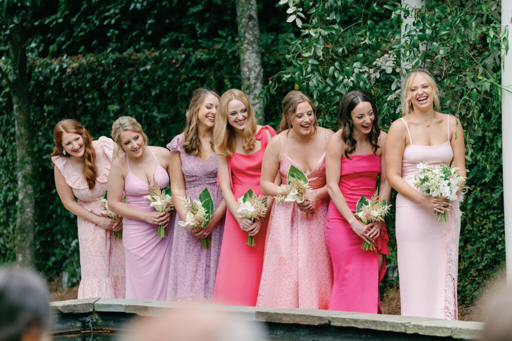 Bridesmaids laugh during wedding ceremony. Bridesmaids in pink and purple mix-matched dresses. 