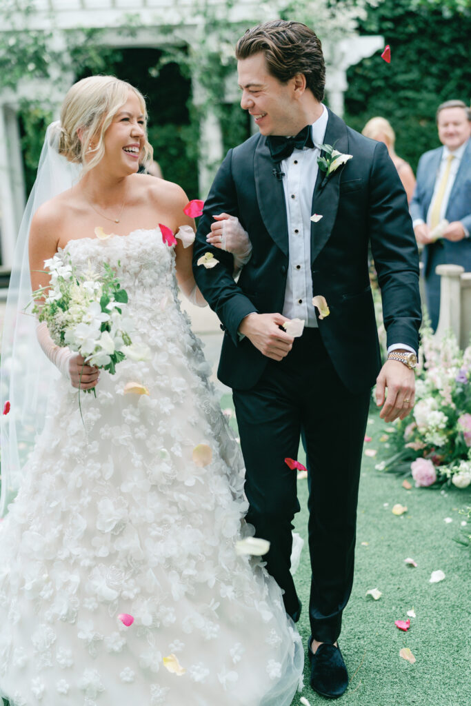 Bride and groom walk down the aisle with pink and white flower petals hitting them. 