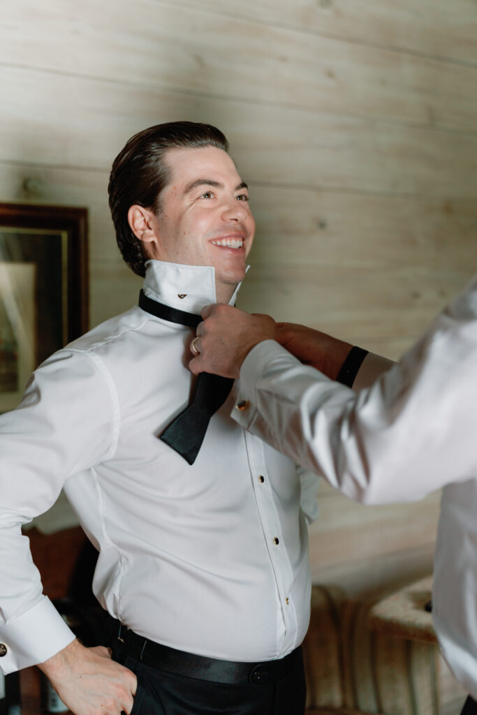 Groom getting help putting on bowtie from groomsman. Charleston photographer wedding