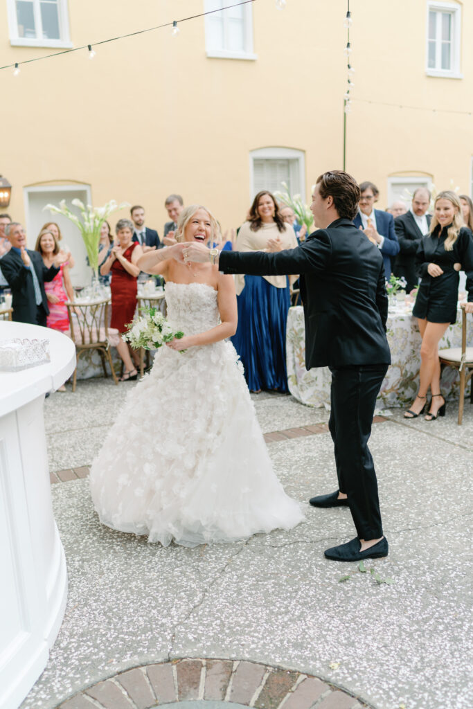 Groom spins bride around with wedding guests laughing and cheering