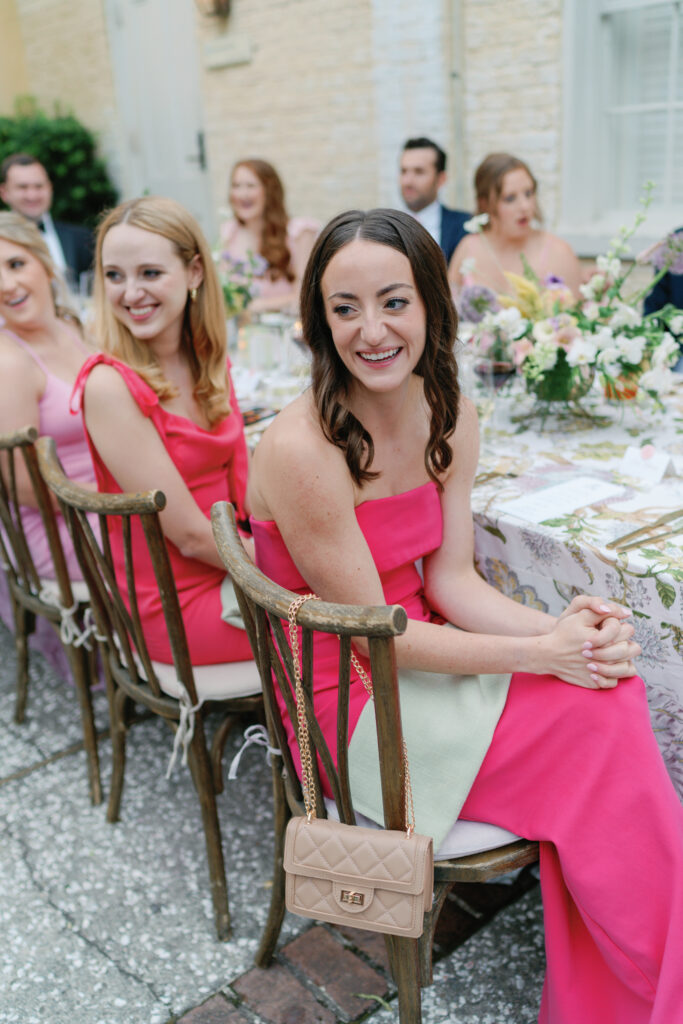 Bridesmaid smiles during speeches at wedding reception. Bridesmaid in bold pink dress.