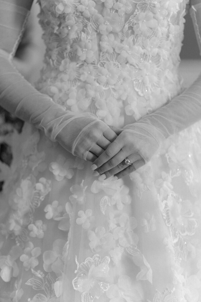 Bride holds hands in on another with sheer sleeves and dress design with flowers. photographer charleston.
