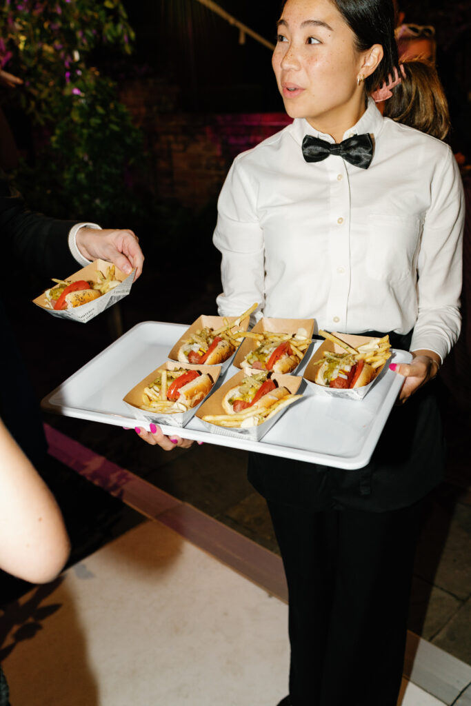 Chicago-style hot dogs late night wedding food. wedding guest grabs a tray with french fries. 