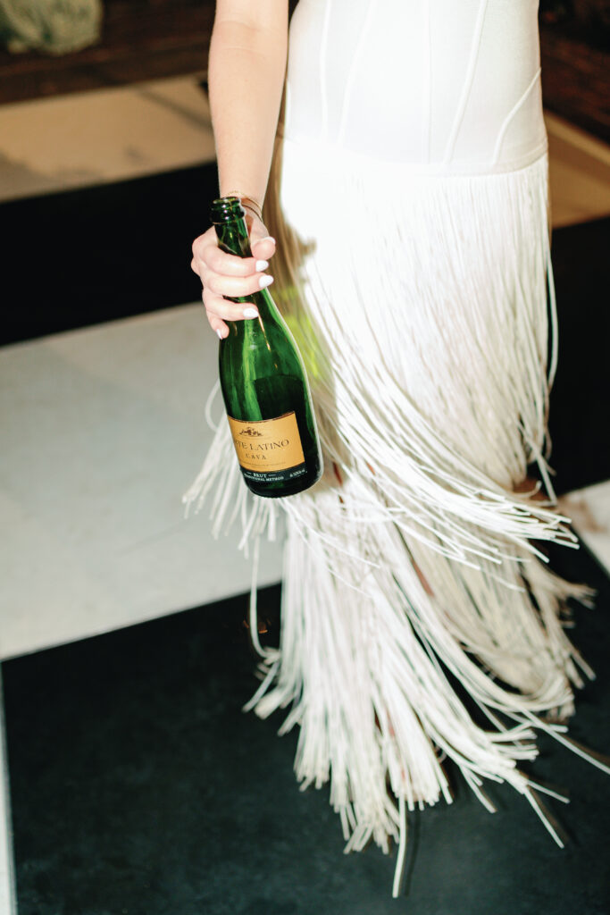 Bride holding champagne bottle with long fringe second dress. Charleston spring wedding. 