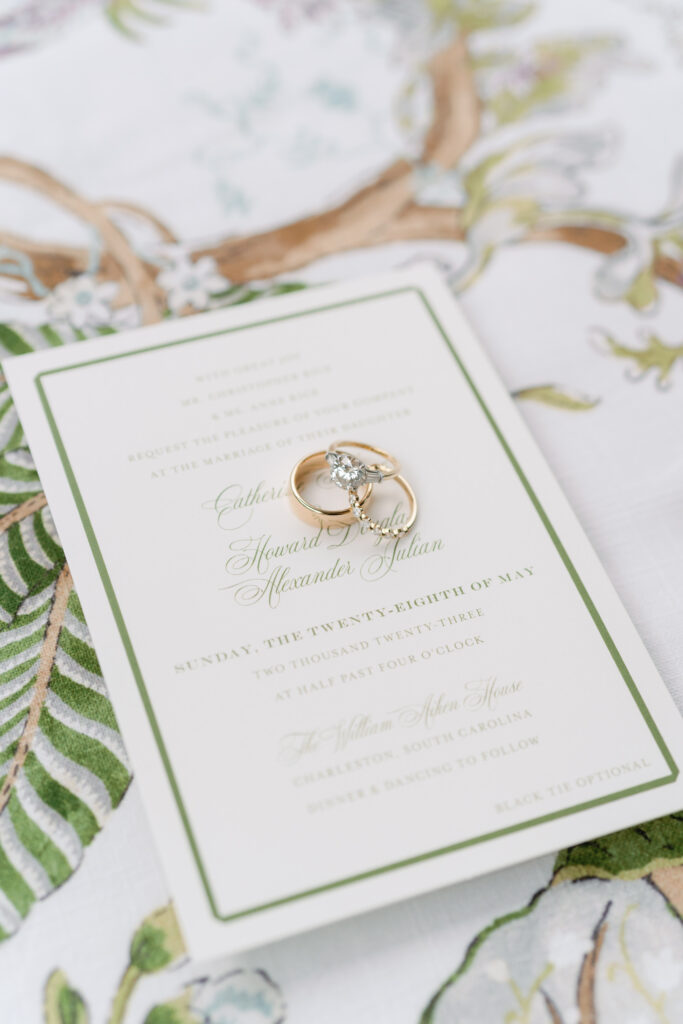 Wedding rings sitting on green and white wedding invitation.