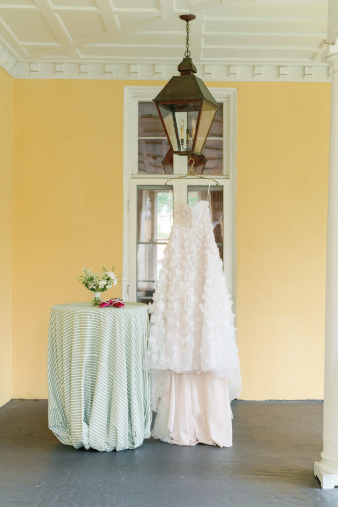 Flower embellished wedding dress hanging from lantern with yellow wall in the background. 