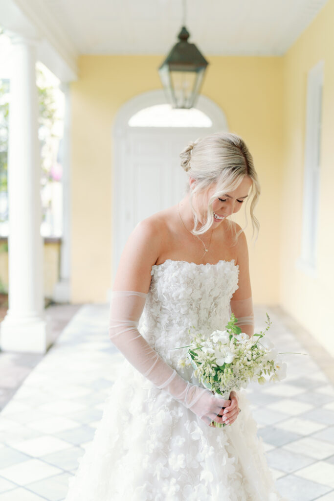 Bride in strapless dress giggles down at small white and green bouquet.