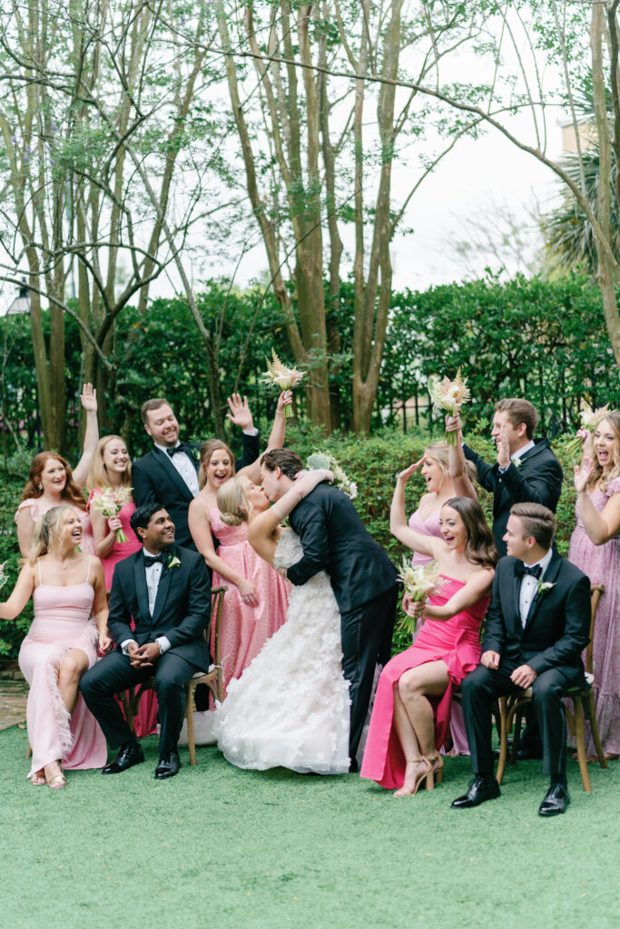 Bridal party group photo. Groom dips bride back for a kiss and wedding party celebrates. 