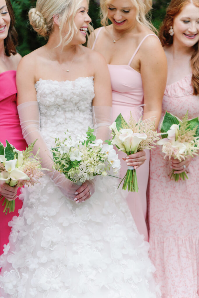 Bridesmaids in mix-matched pink and purple dresses with simple white flowers. 