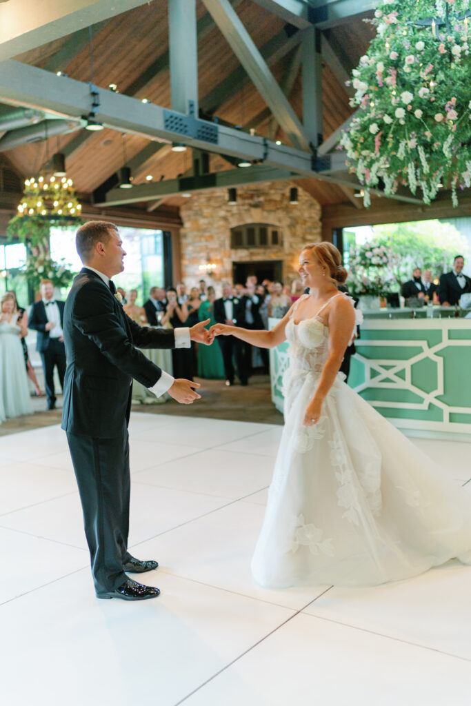 Bride and groom start first dance on all-white dance floor.