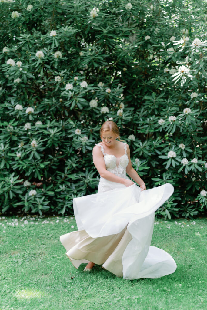 Bride twirls wedding dress in front of bushes with white flowers. 