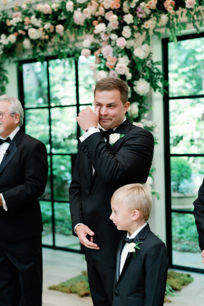 Groom wipes away tear during wedding ceremony. 