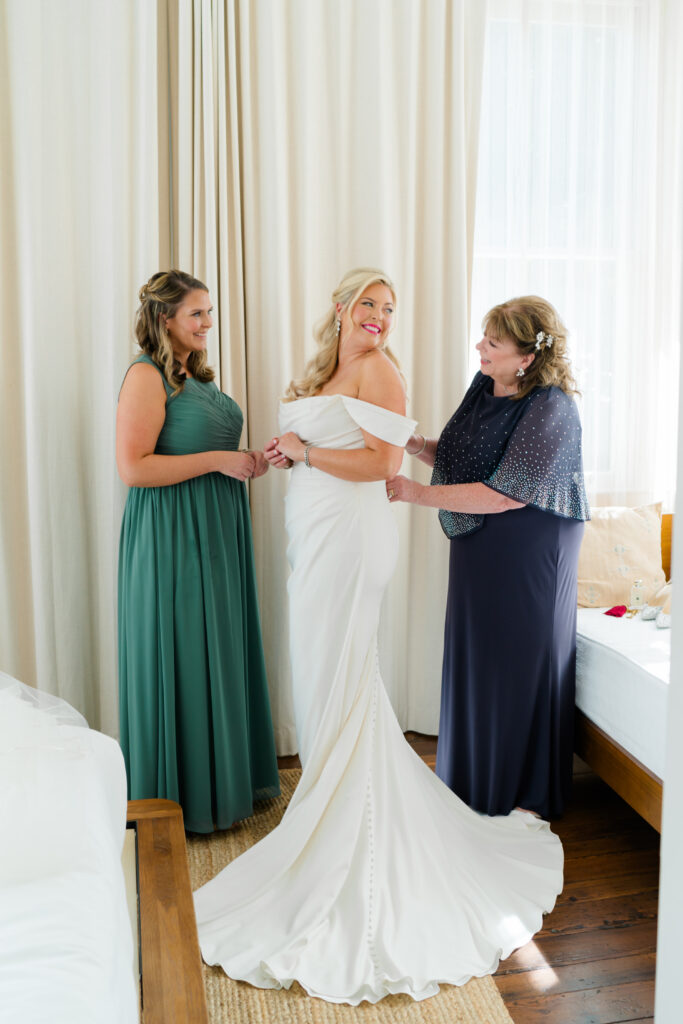 Mother of the bride zips up wedding dress with sister. 