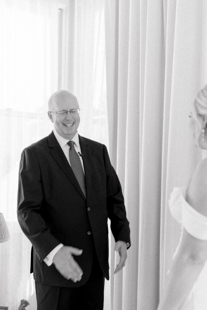 Black and white candid photo of father of the bride seeing his daughter in wedding dress for the first time. 